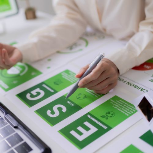Hände markieren ESG Grafiken auf ausgedruckten Unterlagen neben einem Laptop.