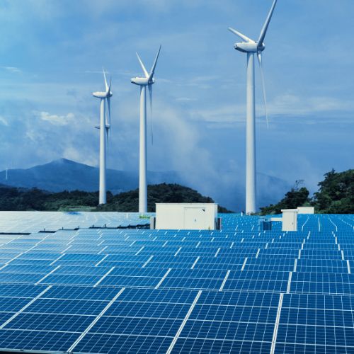 Photovoltaikanlage im Vordergrund mit drei Windrädern vor Bergen und Himmel.